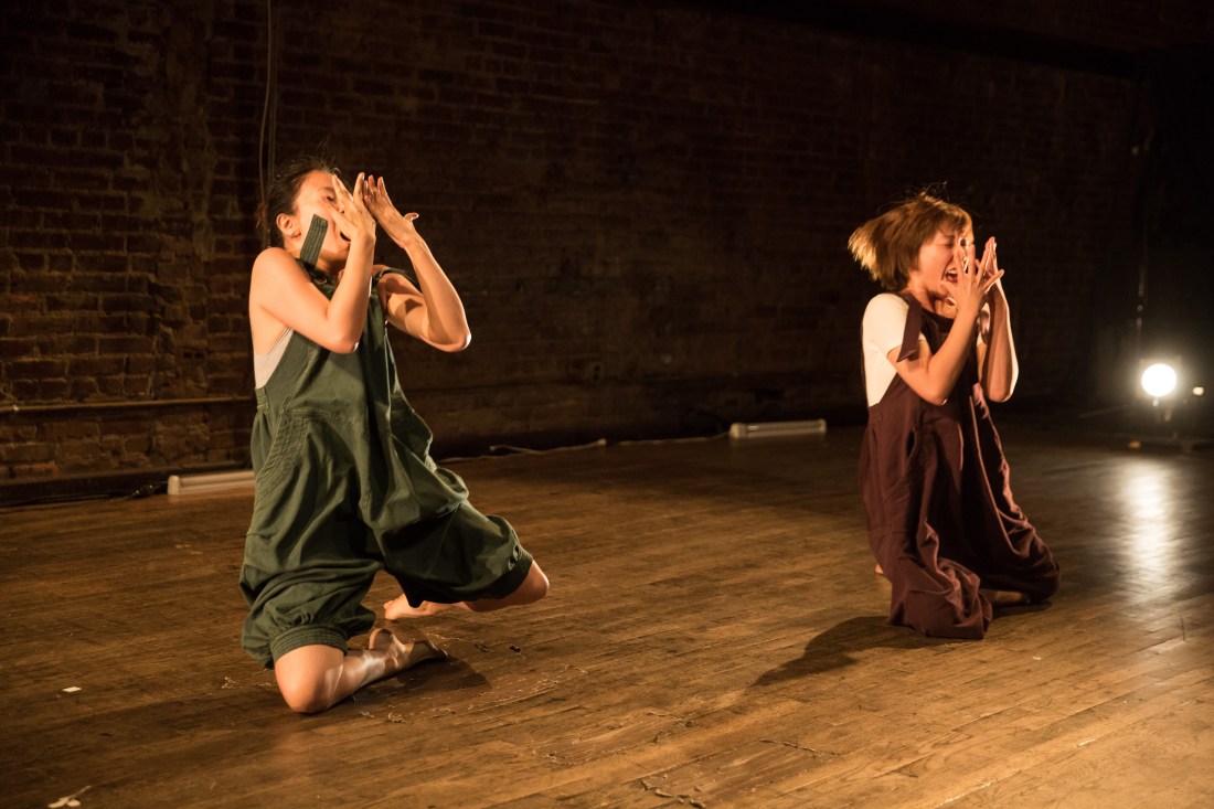 Two performers kneeling with their hands folded over their faces.